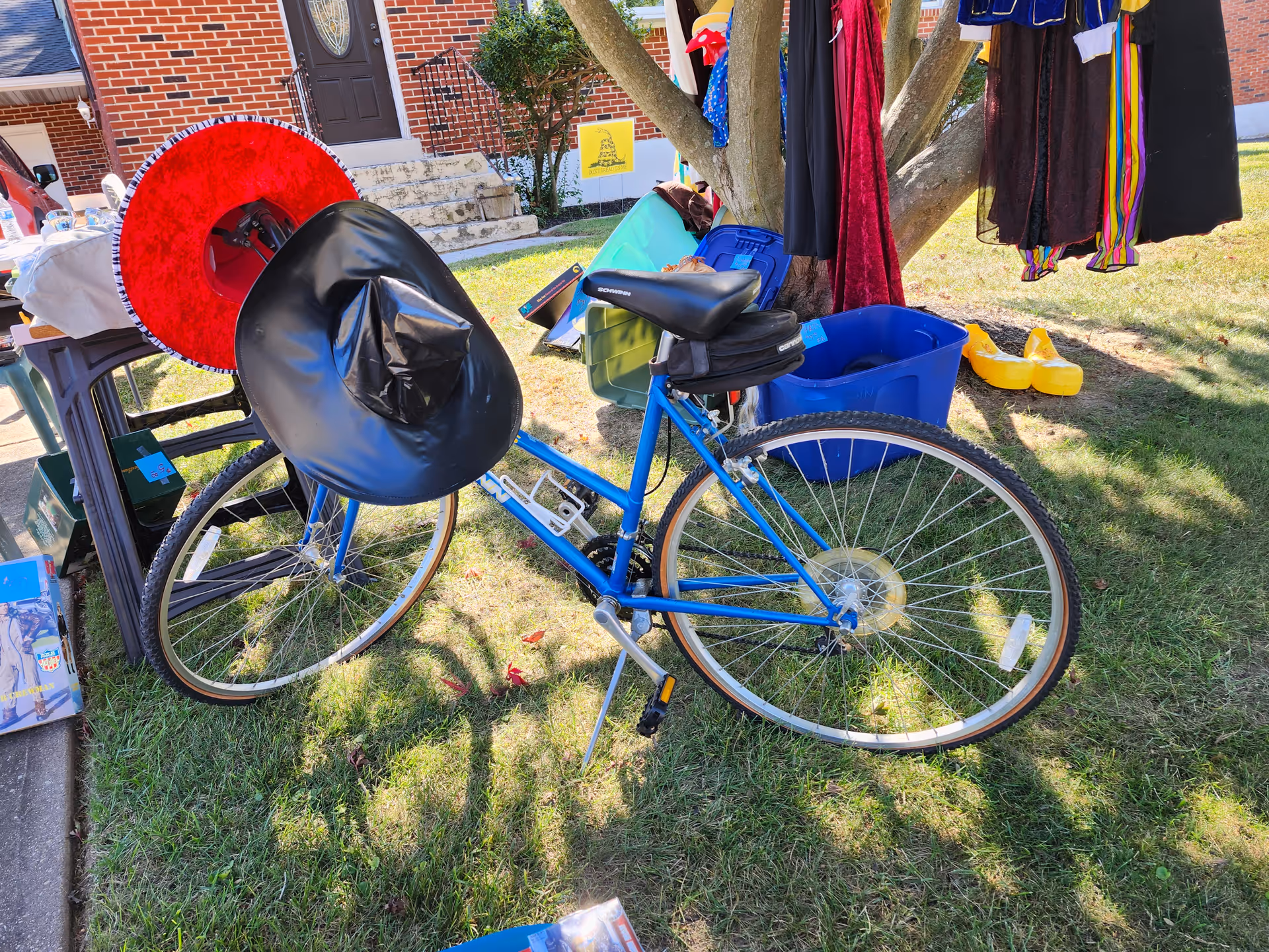 Blue bicycle with a black seat cover on a grassy yard beside a brick house.