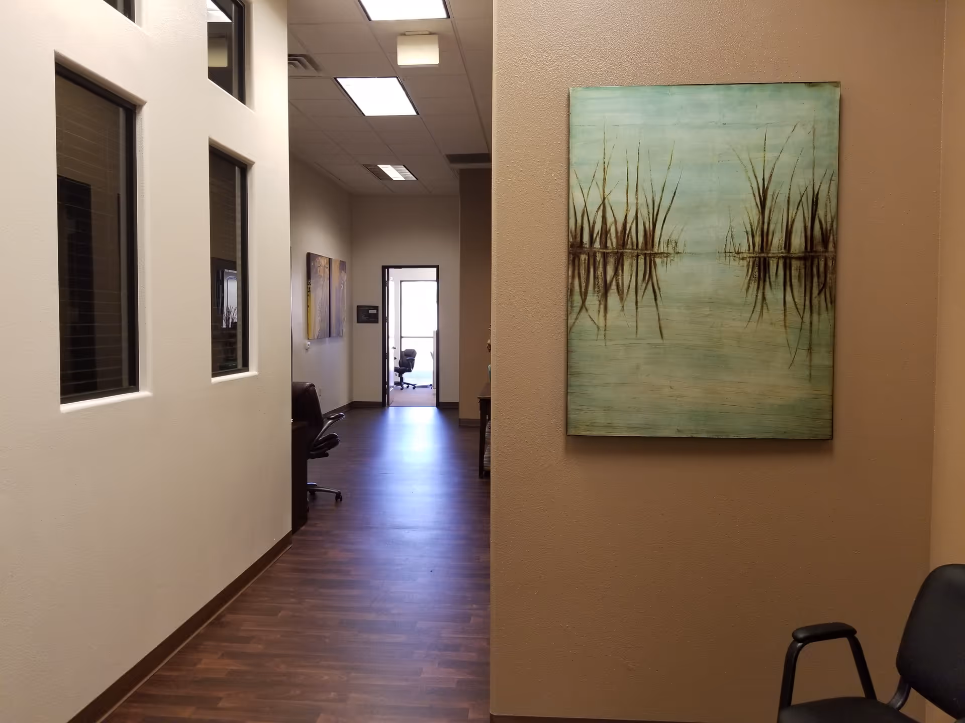 Hallway of a senior living facility with wood floor, beige walls, and a large wall painting.