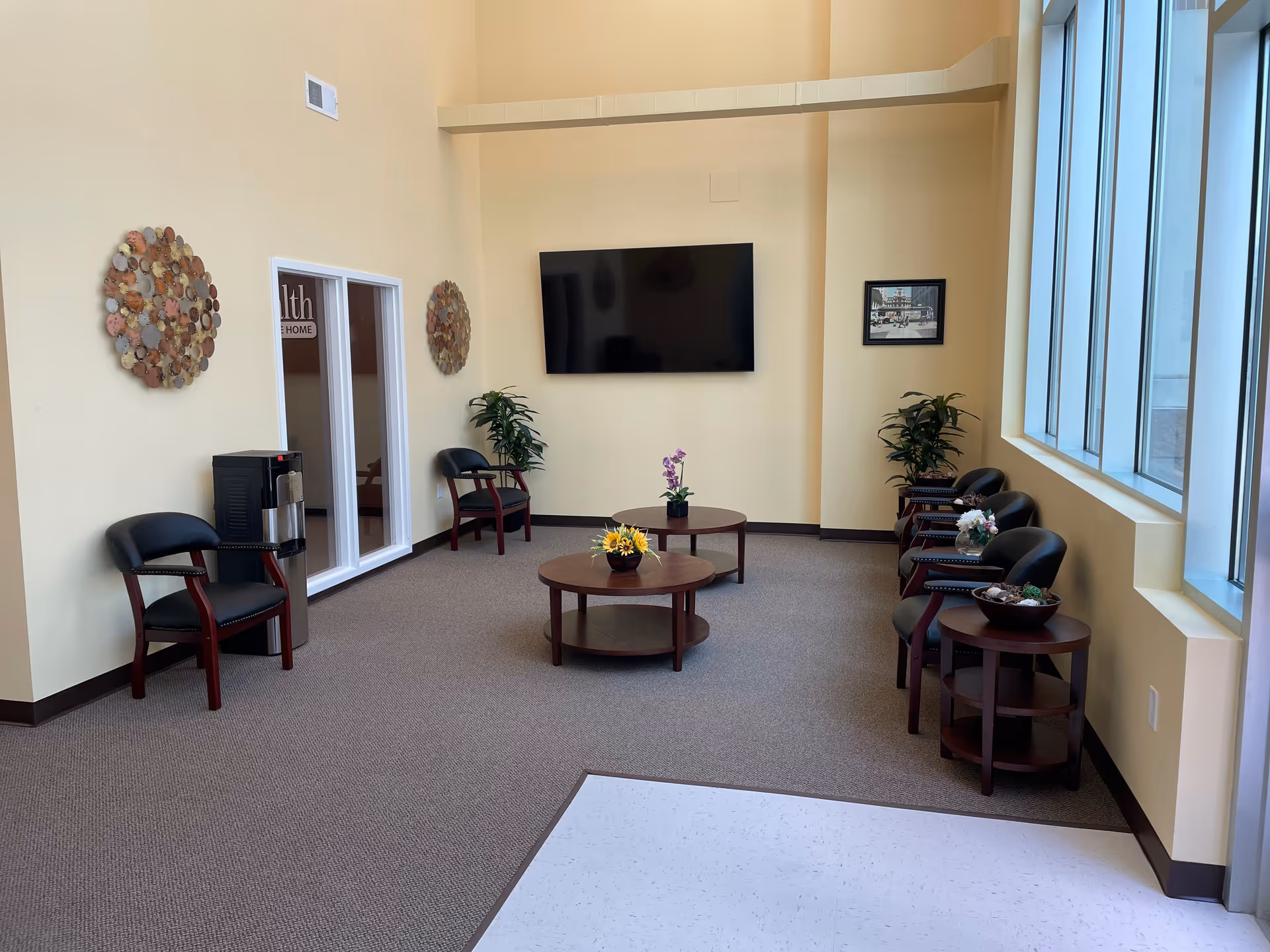 Lounge seating area inside a facility with chairs, tables, and a wall-mounted TV.