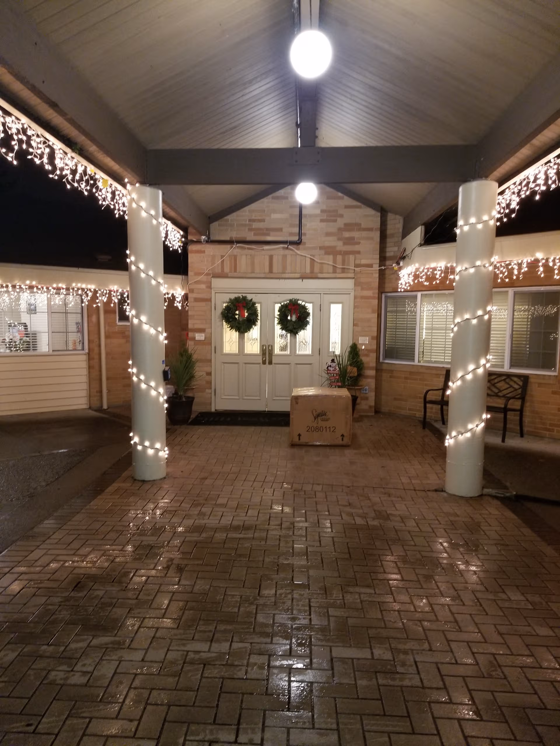 Nighttime exterior of a senior living facility entrance with wreaths and string lights.