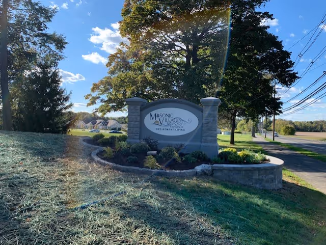 Stone entrance sign for Masonic Village retirement community with landscaped island at street.