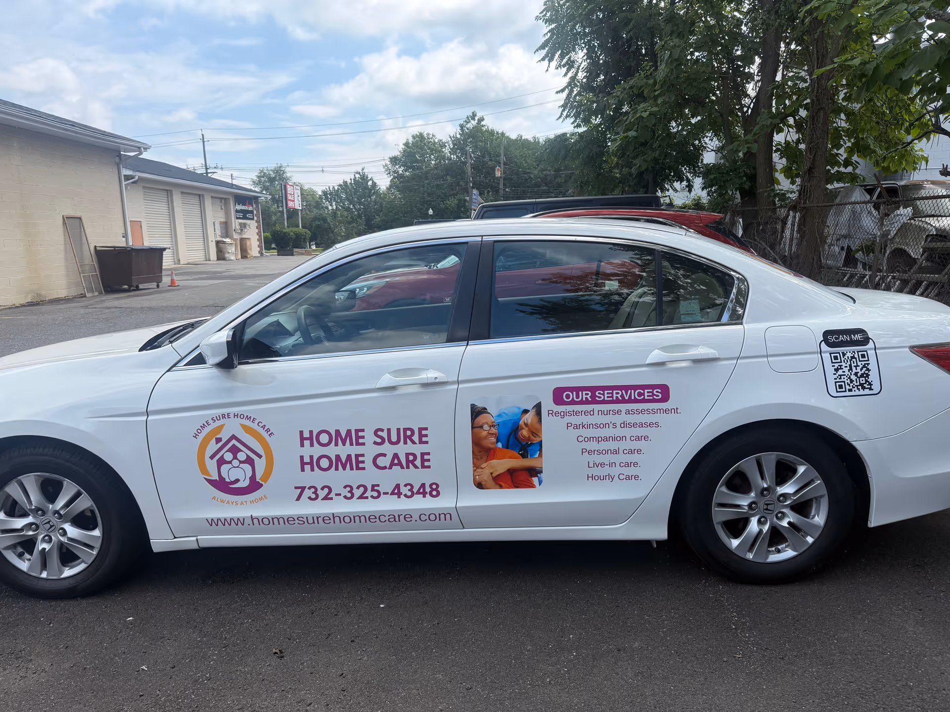 White sedan with Home Sure Home Care branding parked outside a beige commercial building.