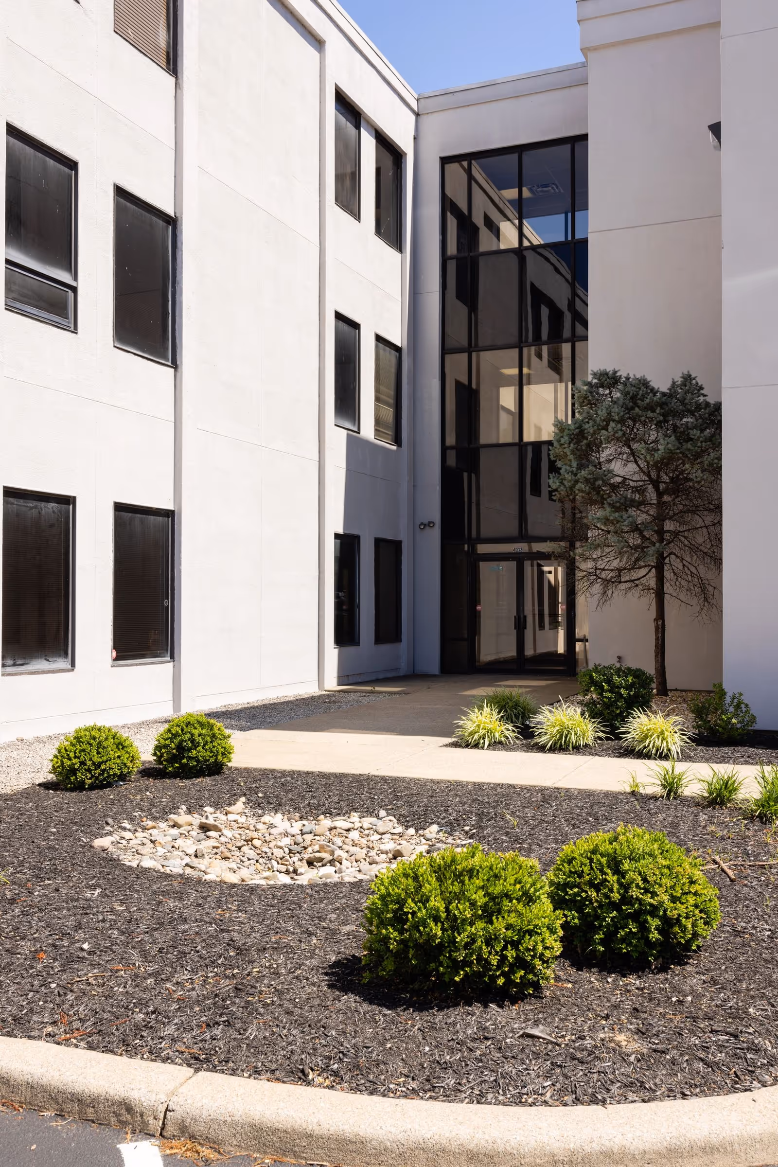 Modern white senior living facility exterior with glass entrance and landscaped front yard.