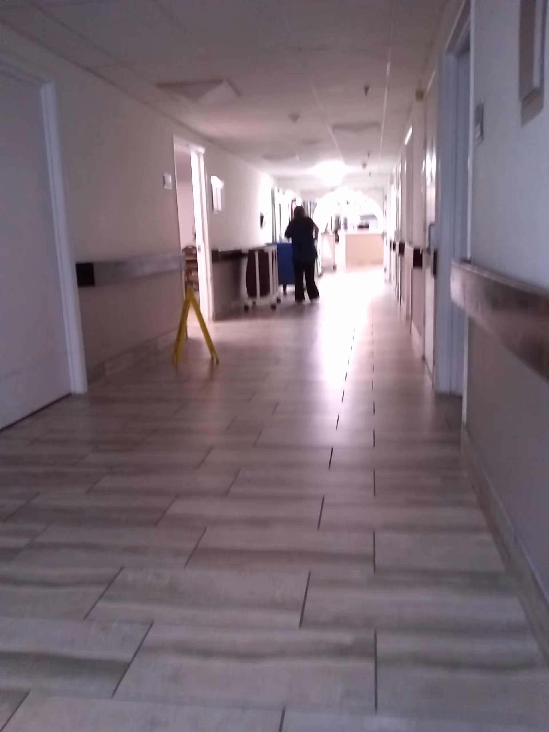 Long, well-lit hallway in Brentwood Place One with carts and a distant figure.
