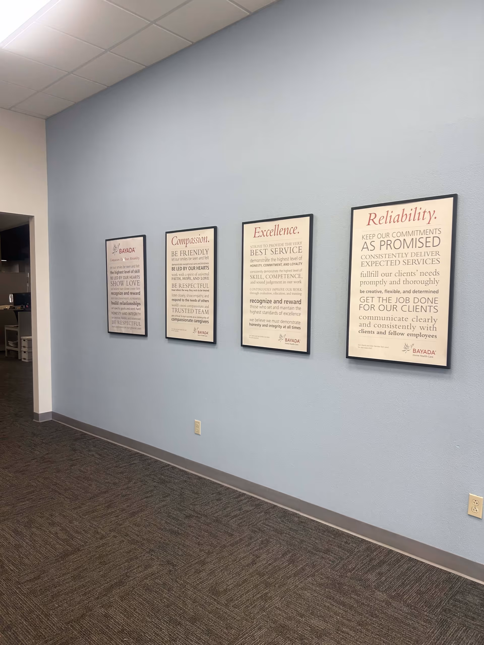 Blue hallway with framed posters on the wall in a senior living facility.
