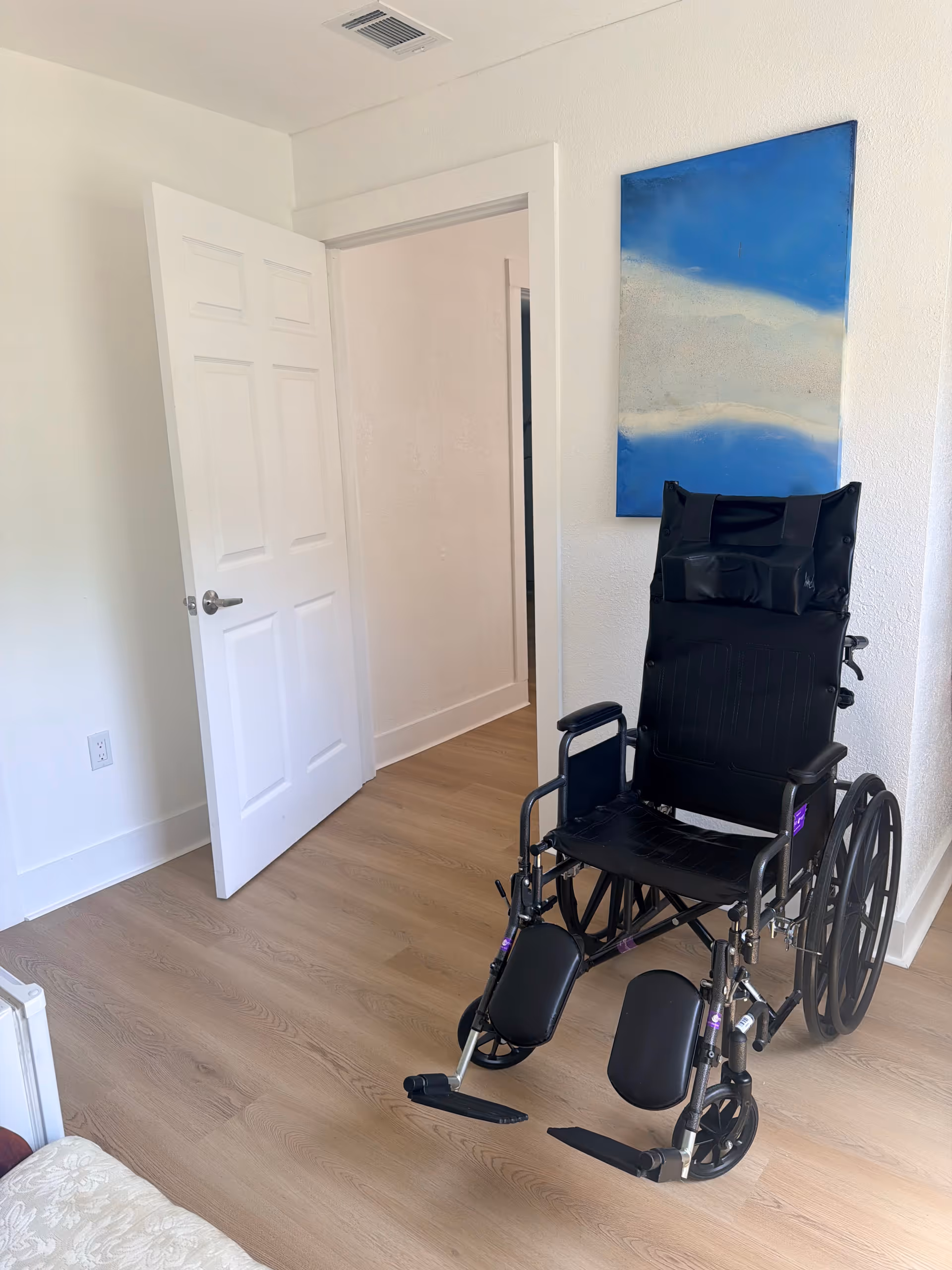 Black wheelchair in a bright room with an open door and a blue abstract painting.