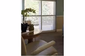 Sunlit lounge in a nursing center with a round table, potted plant, and blinds.