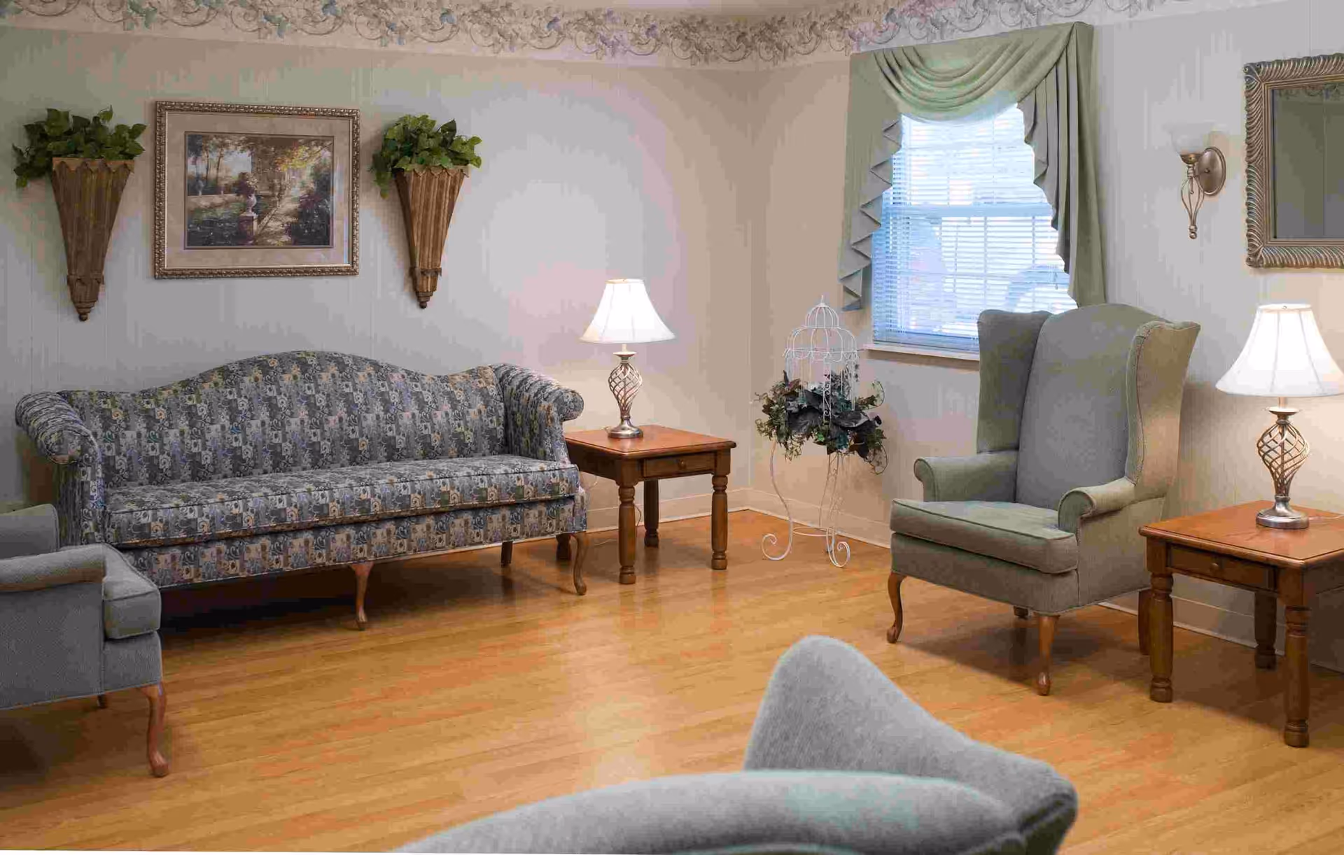 Cozy senior living lounge with patterned sofa, armchairs, lamps, and a window.