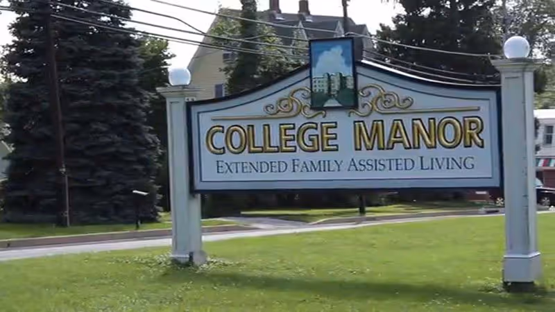 An outdoor sign reading College Manor Extended Family Assisted Living stands on a grassy lawn.