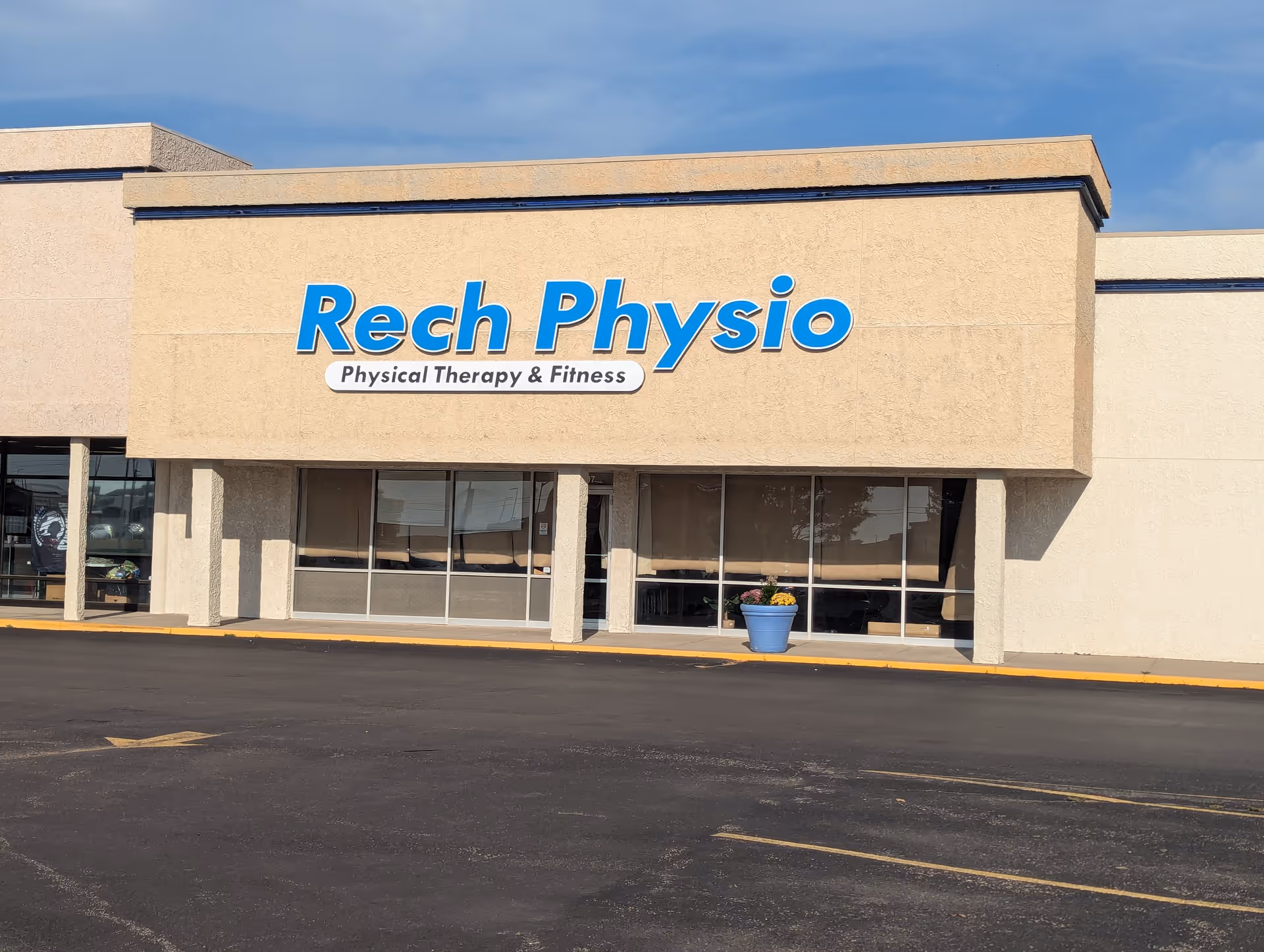 Exterior view of Rech Physio clinic storefront with beige facade and blue sign.