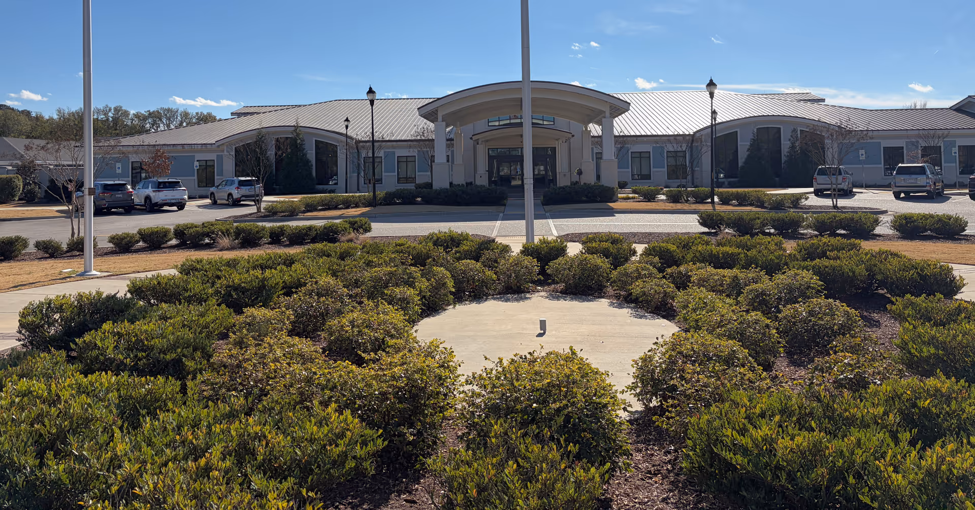 Front view of a single-story Veteran Village senior living facility with curved entrance and parking.