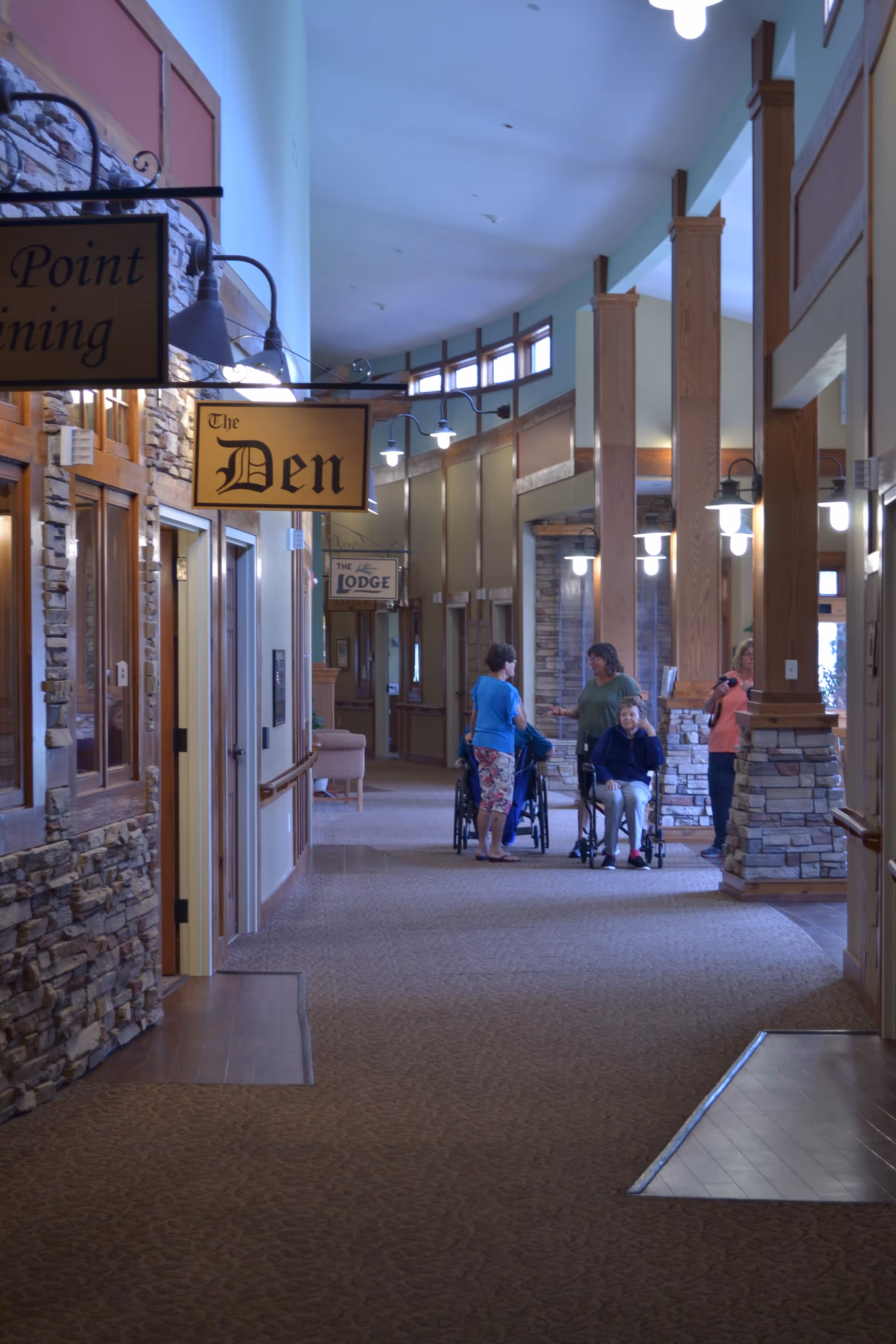 Interior corridor of Warroad Senior Living Center with residents and wheelchairs near signs.