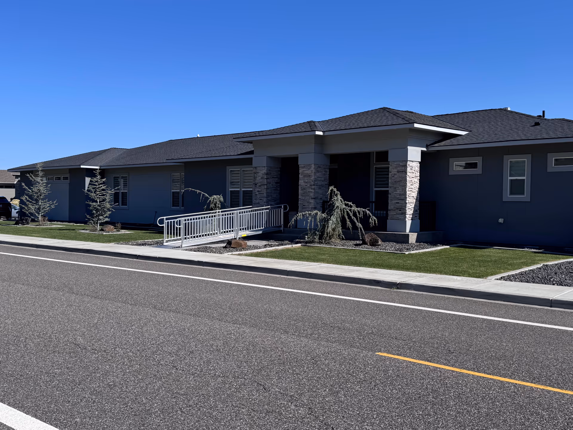 Single-story modern senior living facility exterior with ramped entrance and manicured lawn.