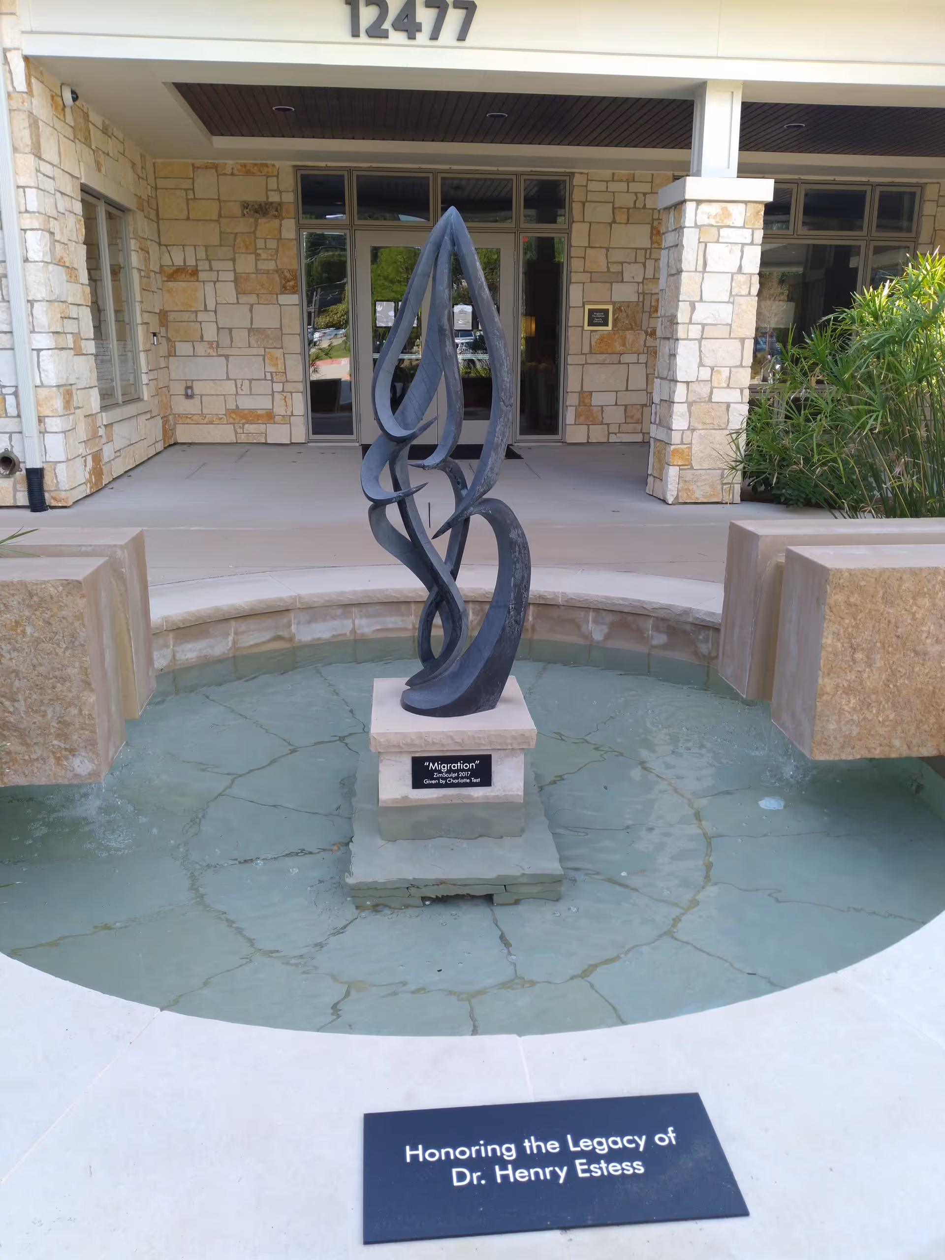 Front entrance of a hospice building with a tall abstract metal sculpture in a circular fountain.