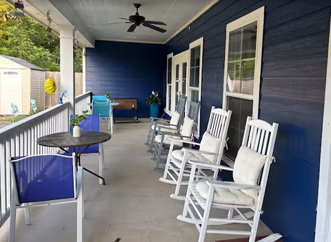 Covered outdoor porch with blue walls, white rocking chairs, and a round table.