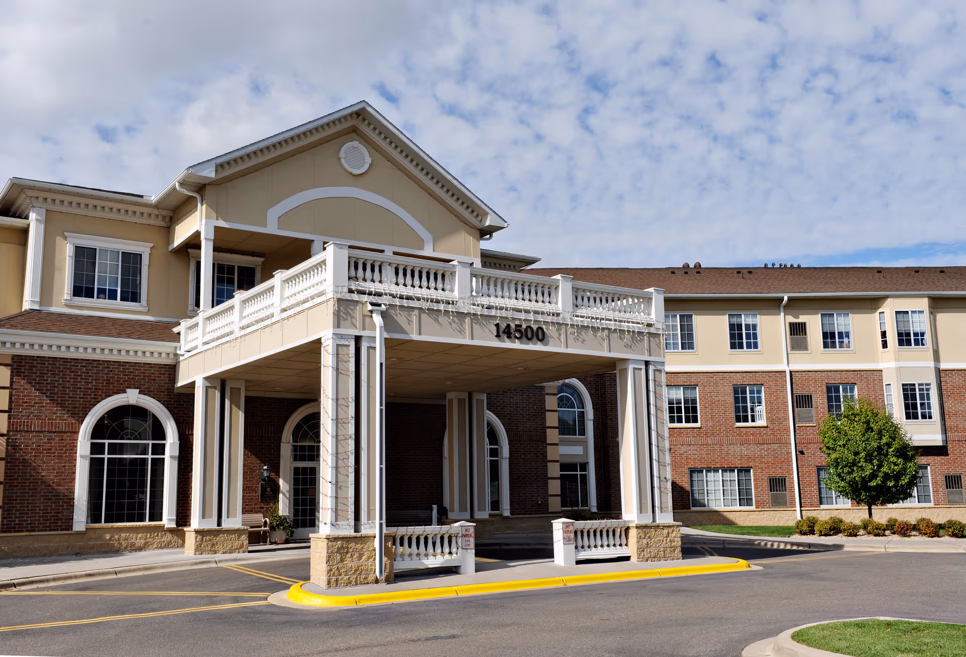 Senior living facility exterior with a covered entrance and brick base.