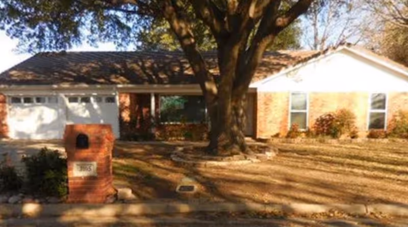 Front exterior of a brick senior living facility with a large tree and driveway.