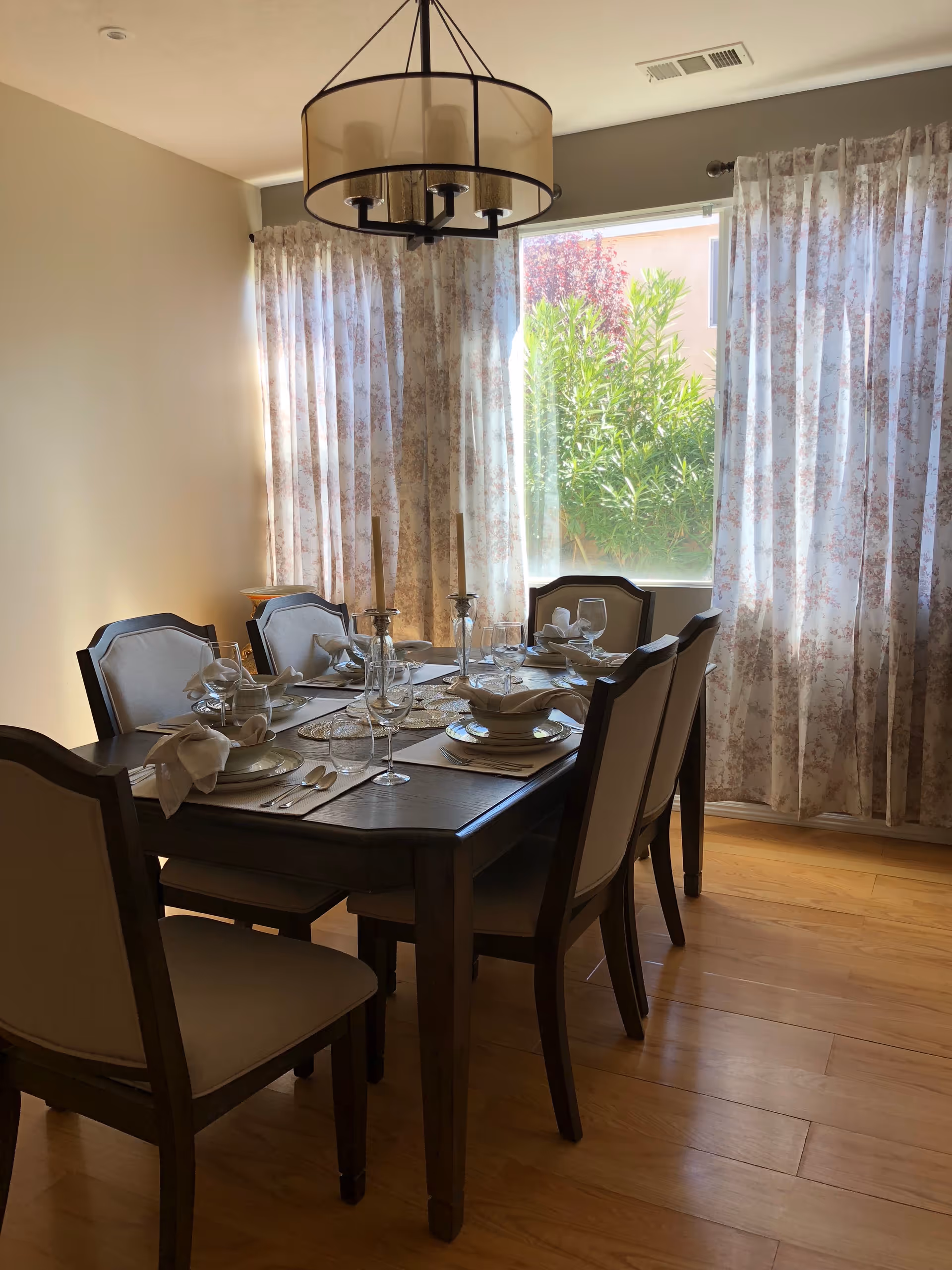 A formal dining table set for a meal in a bright, curtained dining room.