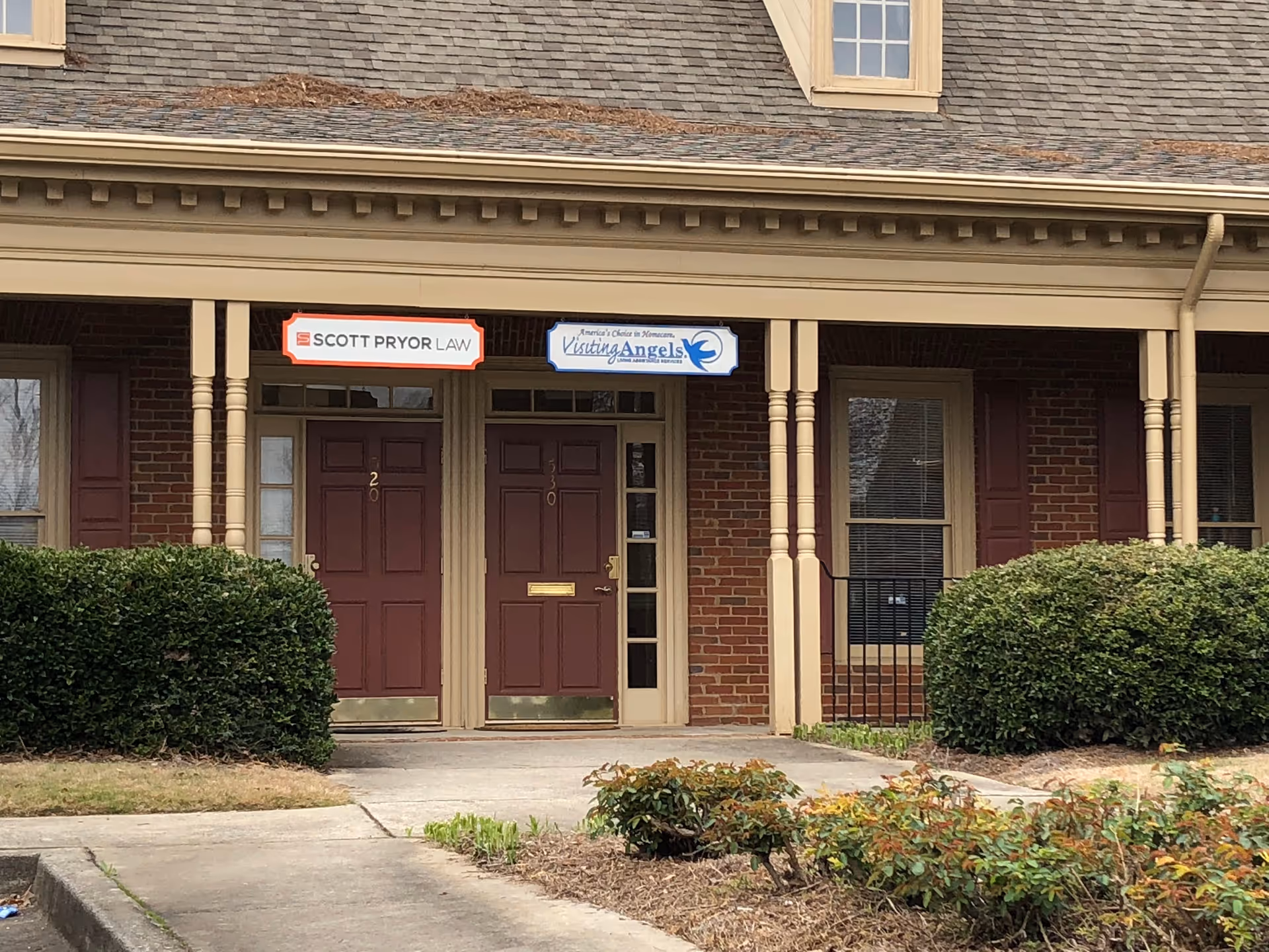 Brick building entrance with columns, double doors, and signs for Visiting Angels and Scott Pryor Law.