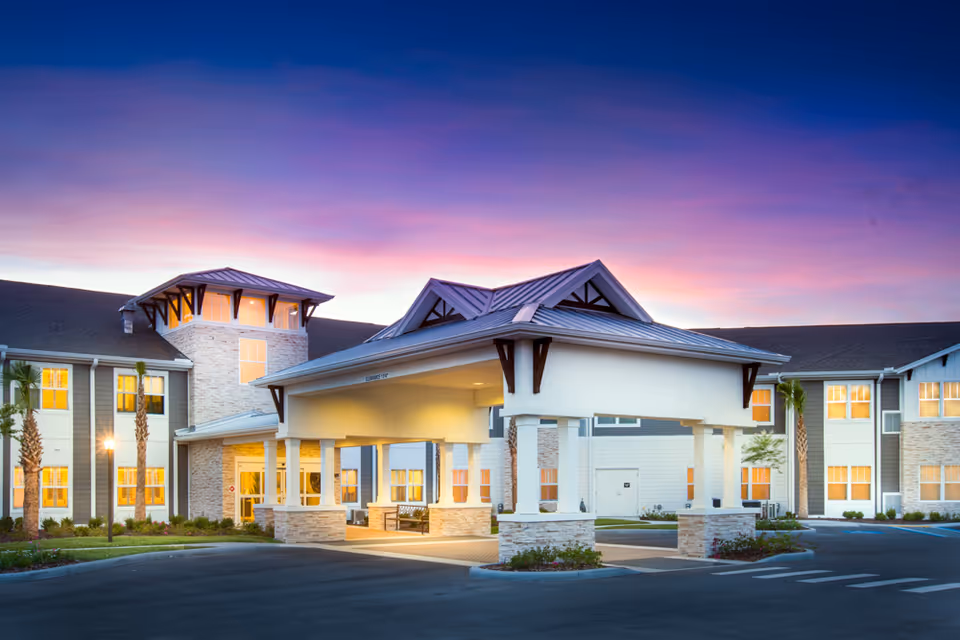 Sunset-lit exterior of The Crossings at Riverview senior living community with a porte-cochere.