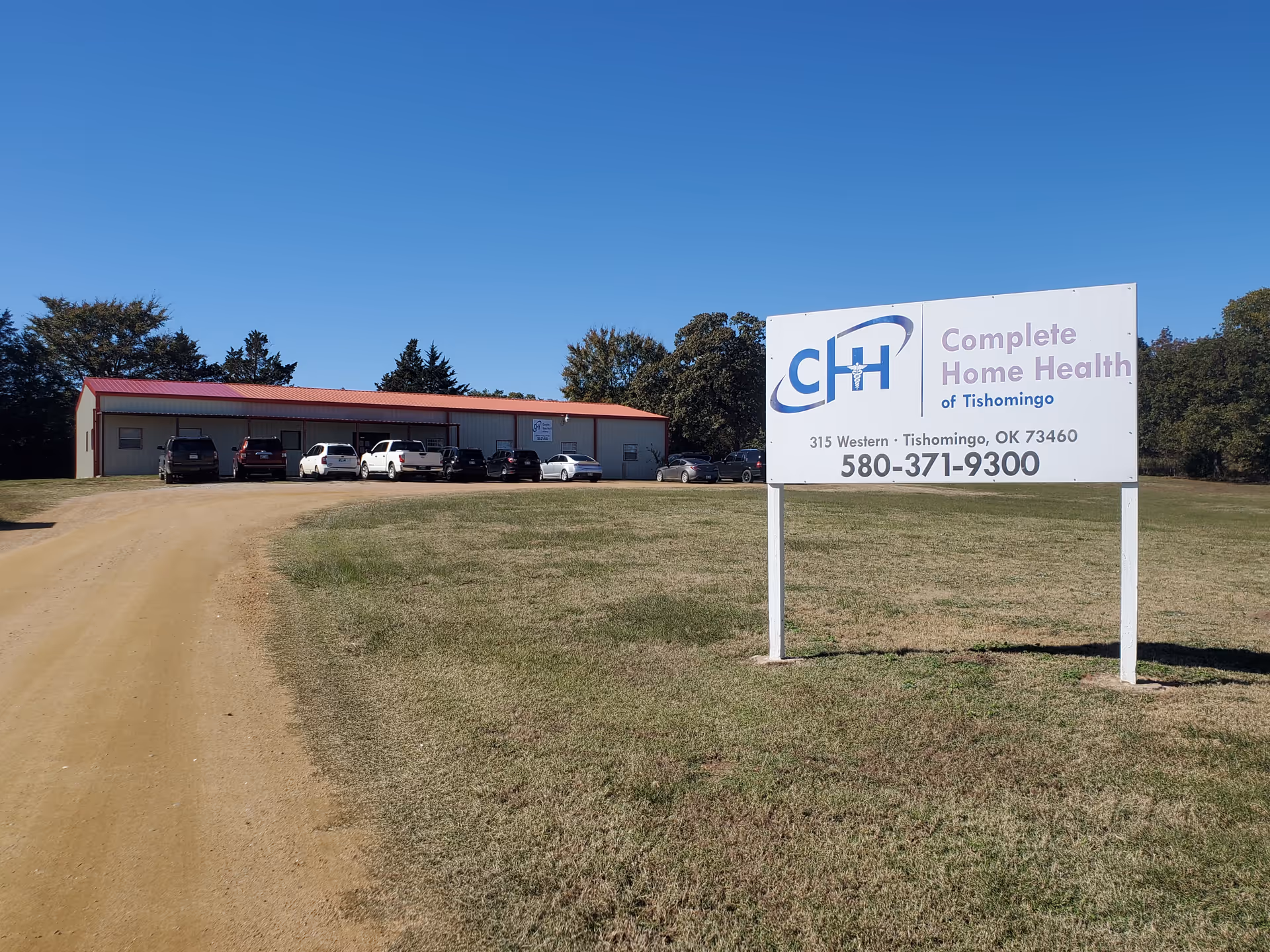 Exterior of a rural healthcare facility with a large sign and parked cars.