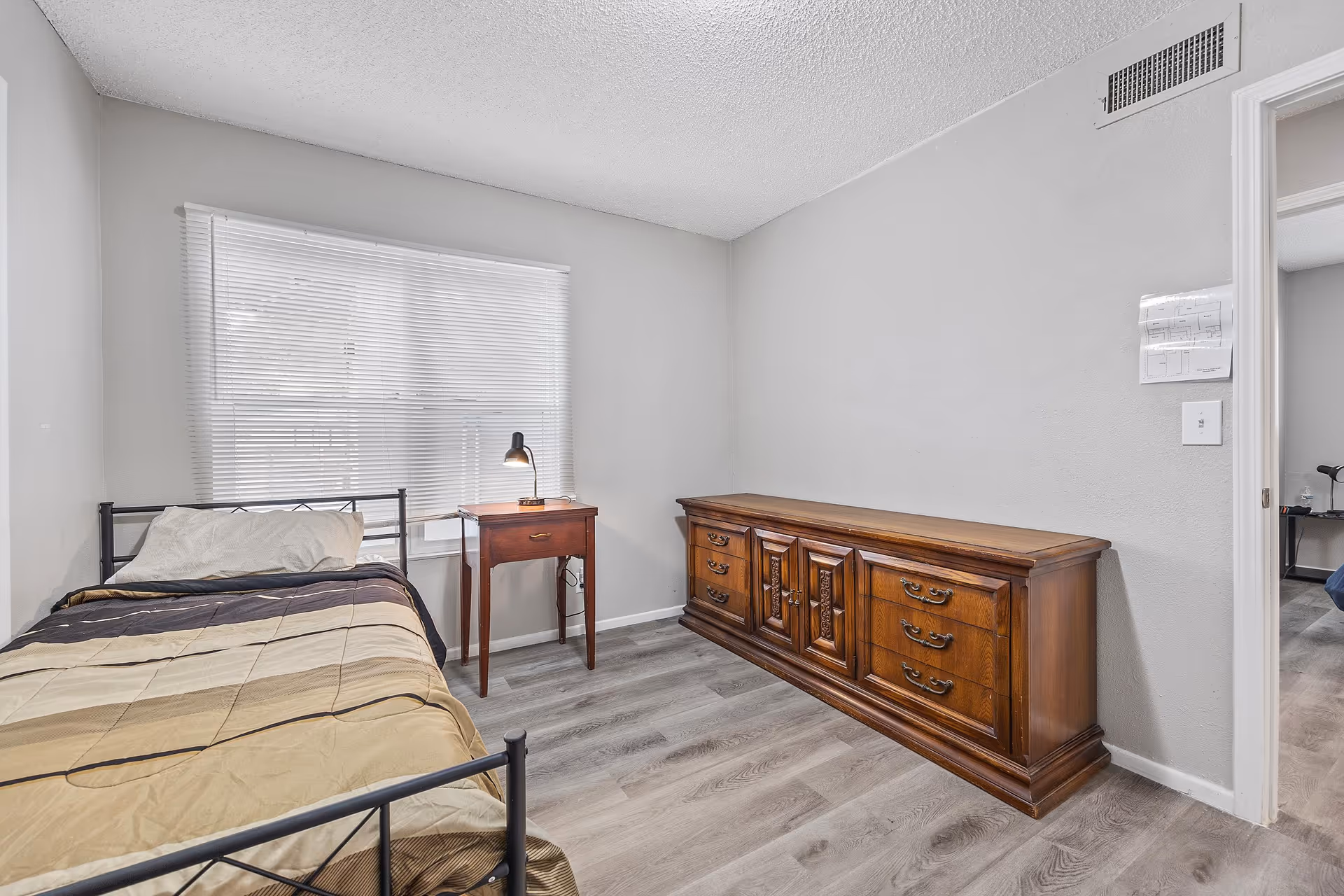 A tidy bedroom with a single bed, nightstand, lamp, and a wooden dresser.