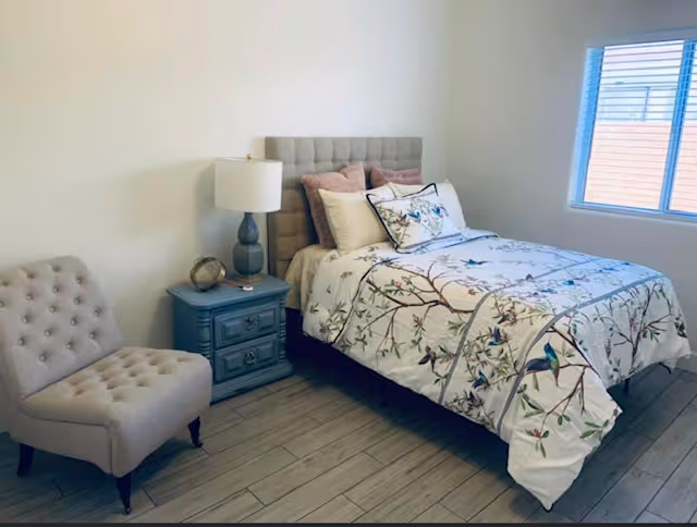 Bedroom with floral comforter, tufted headboard, blue nightstand, lamp, and matching chair.