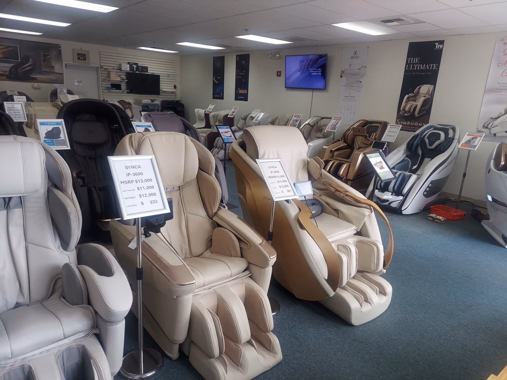 Rows of massage chairs in a showroom with signs and posters on the walls.