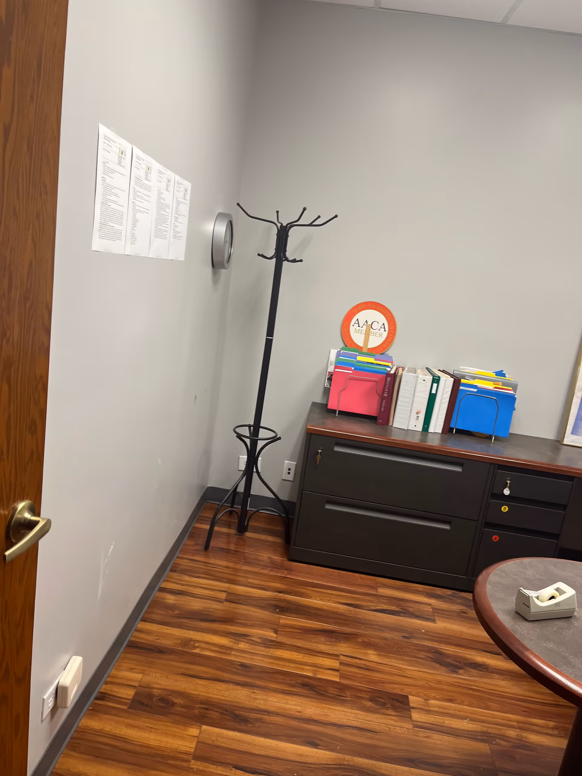 Interior office corner with coat rack, dark filing cabinet, and colorful folders.