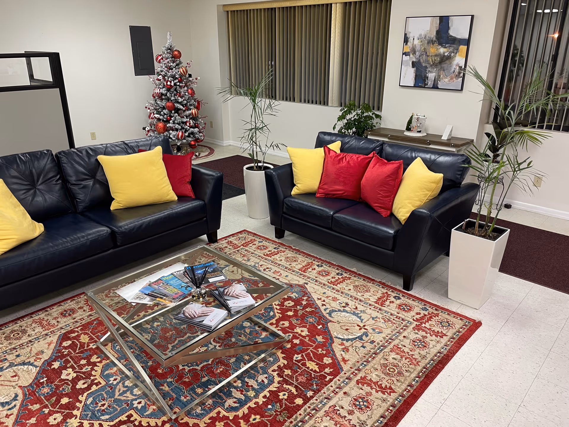 A lounge with black leather sofas, colorful cushions, a glass coffee table, and a Christmas tree.