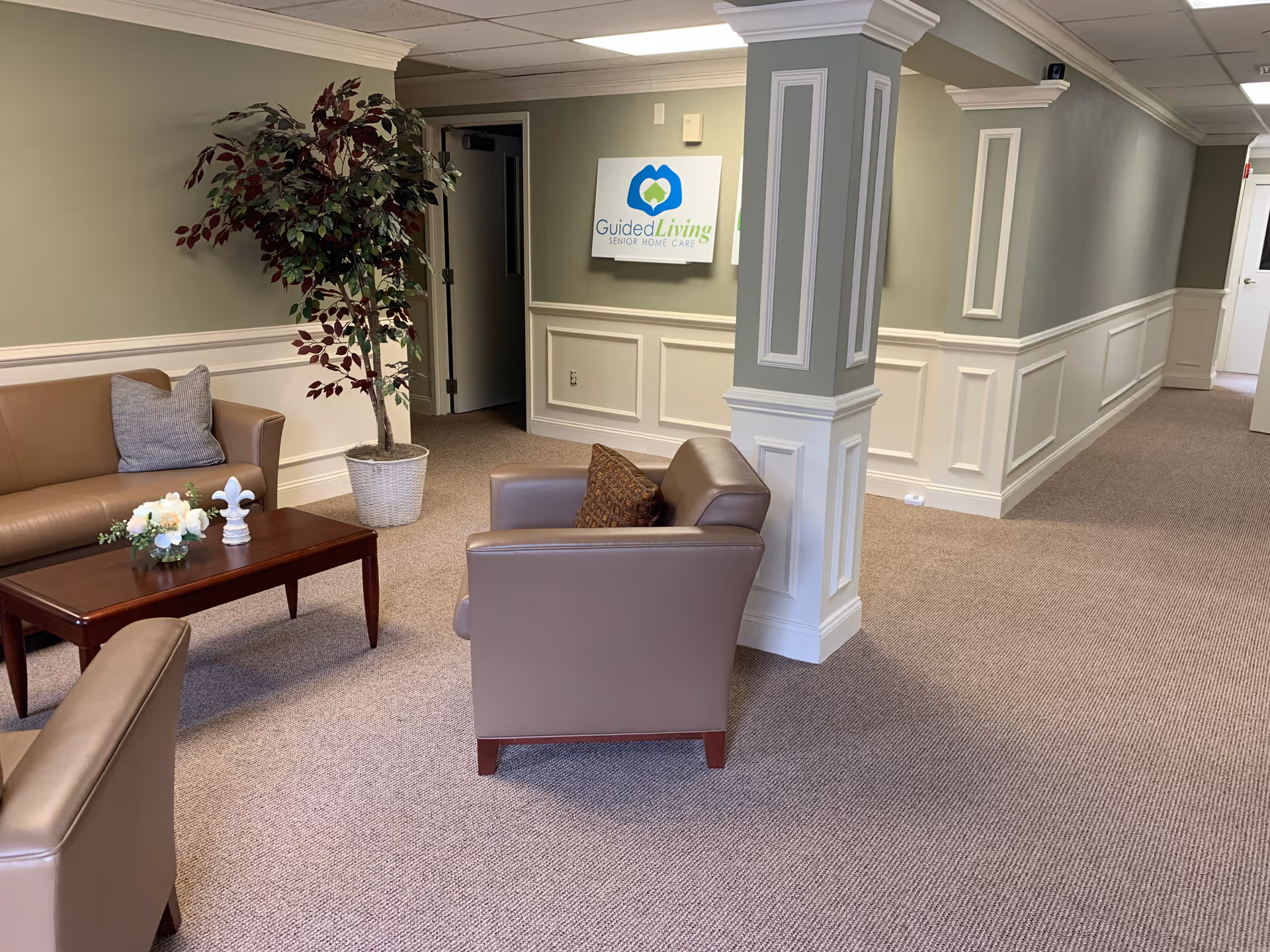 Lobby lounge area with beige seating, a coffee table, plant, and a wall-mounted sign.