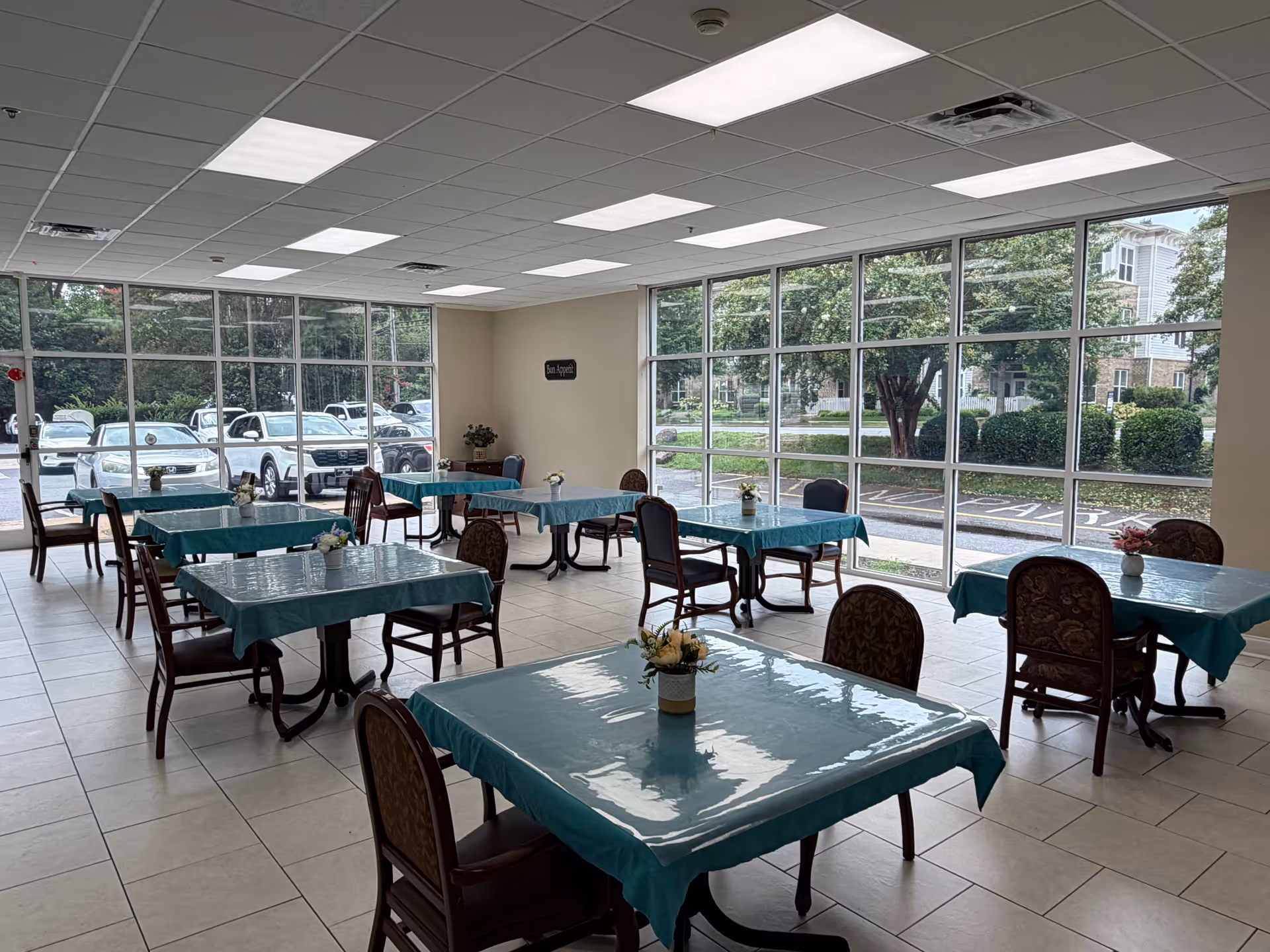 Bright dining room with turquoise tablecloths, several tables, and large windows overlooking outside.