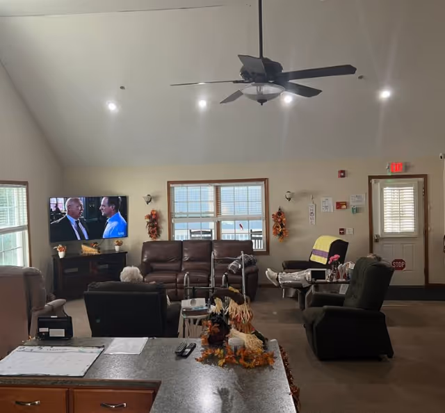 Cozy living room in a senior facility with couches, TV, and windows.