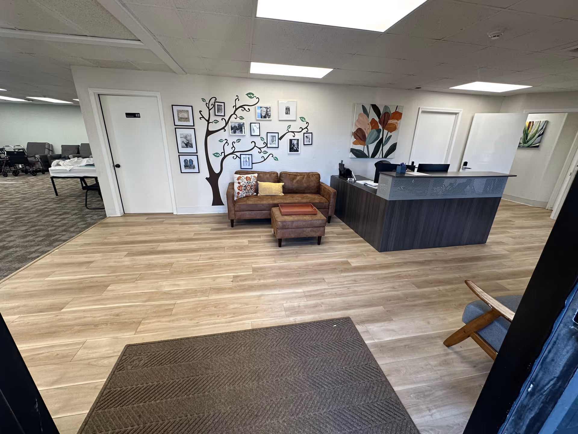 Reception desk with dark wood finish, leather seating, and a tree-wall gallery in a bright lobby.
