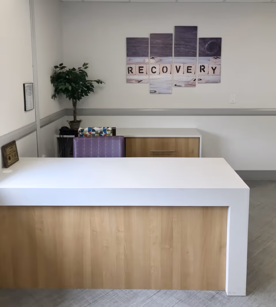 A white and wooden front desk in a medical reception area with a plant.