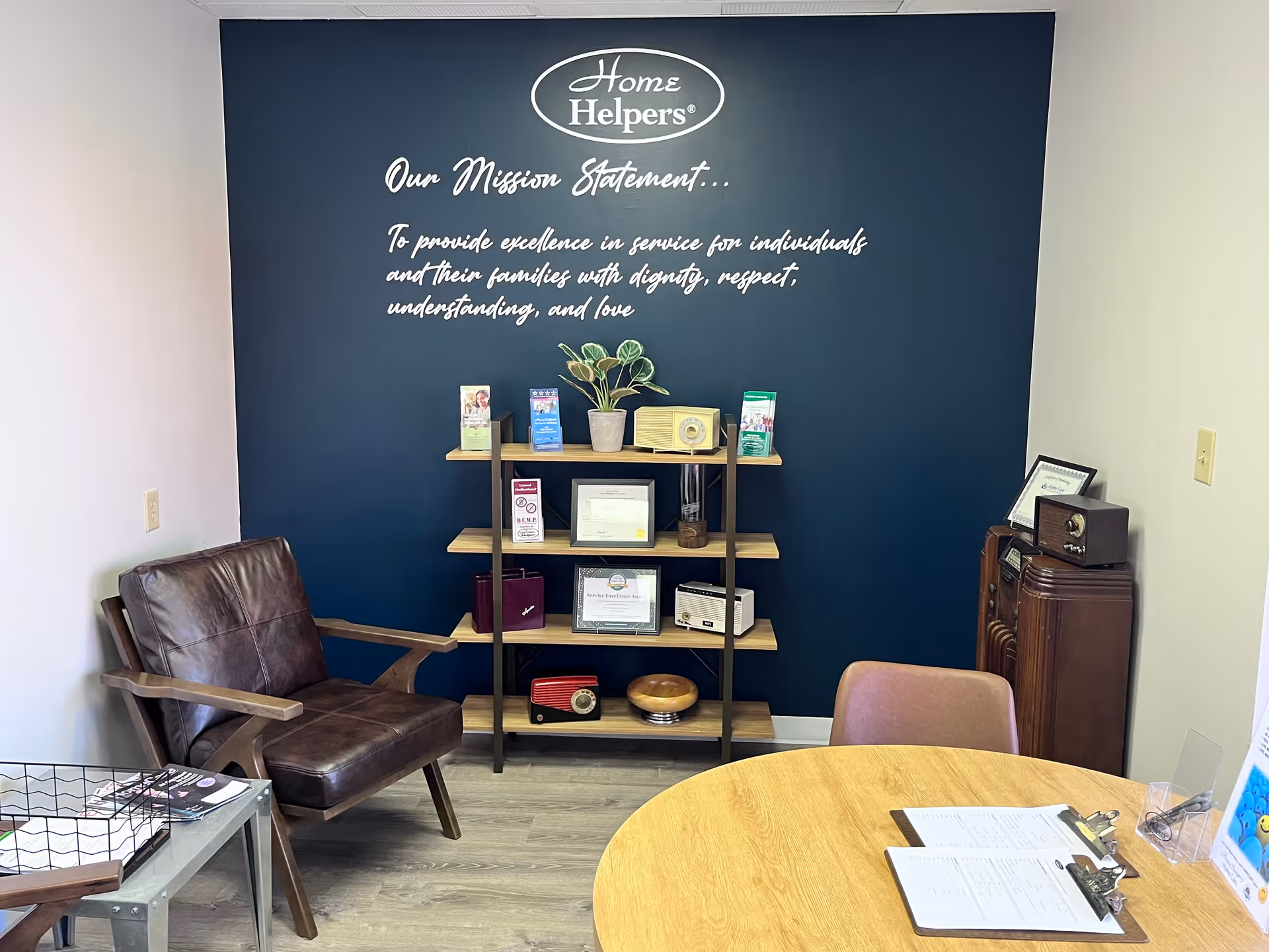 Interior office lounge with blue wall mission statement, bookshelf, leather chair, and round table.