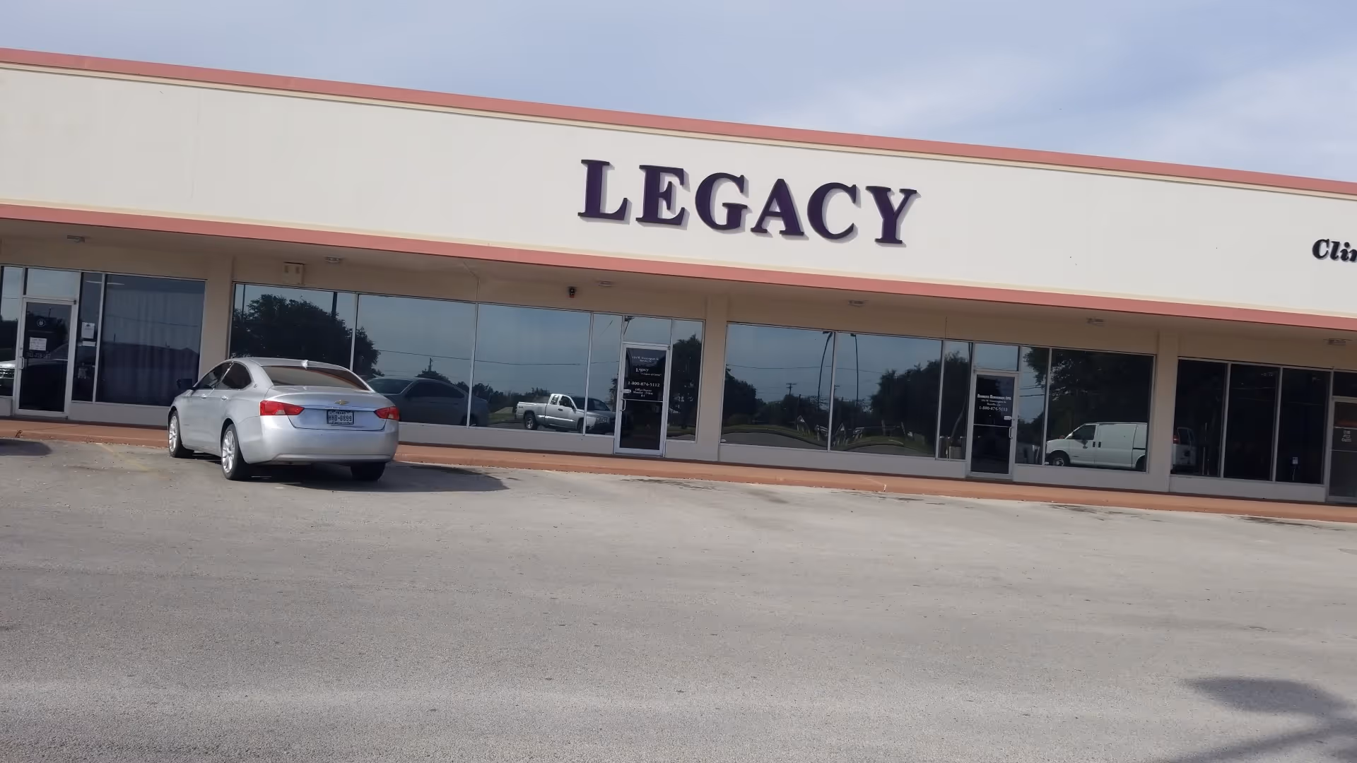 Exterior of Legacy facility with large glass storefront and a parked car.