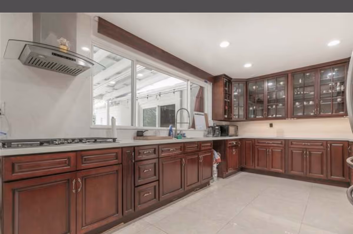 A spacious kitchen with dark wood cabinets, a sink, stove, and glass-fronted upper cabinets.