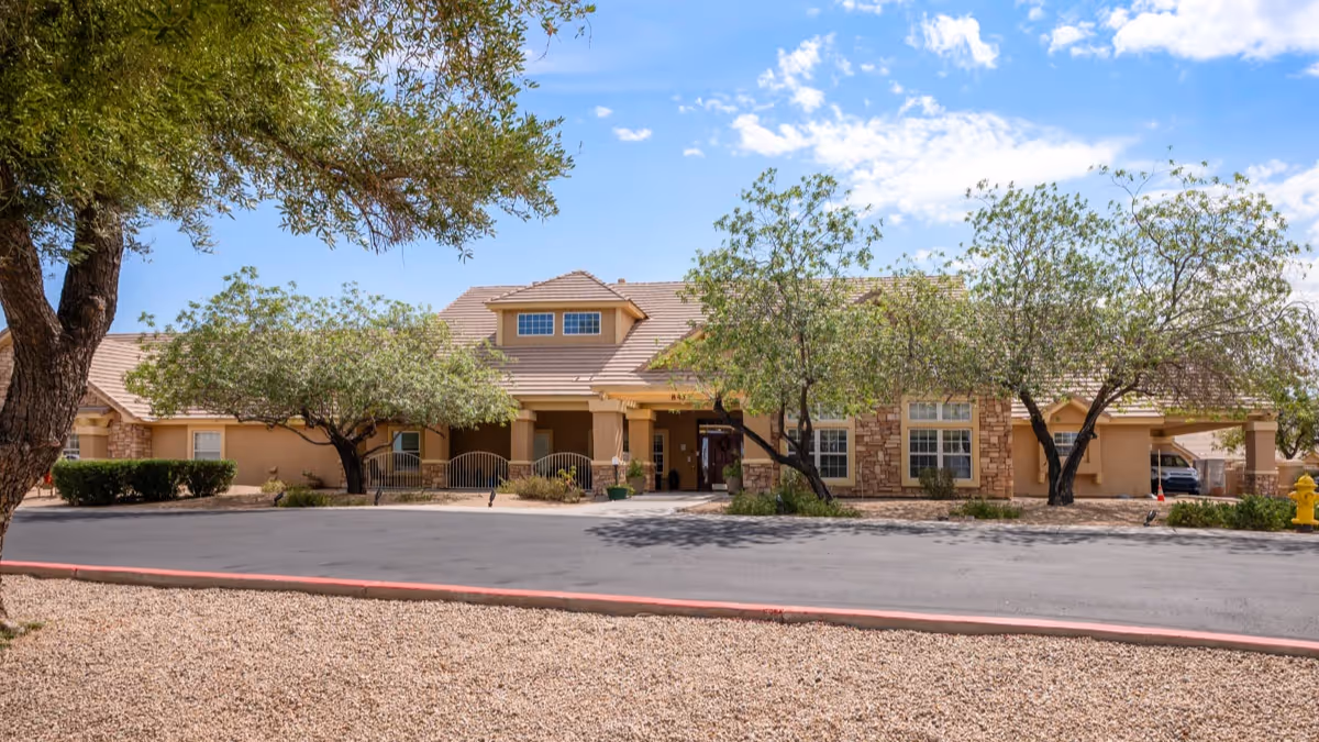 Single-story senior living facility with beige stone facade, parking lot, and trees.