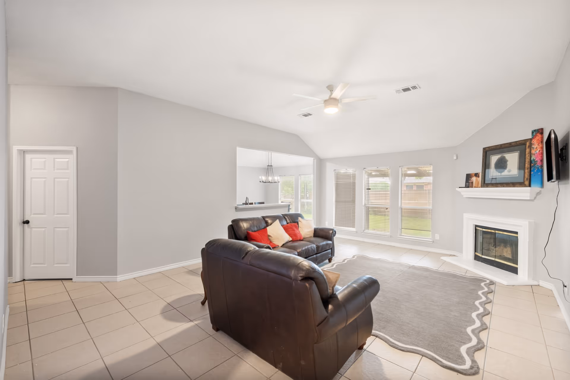 Bright living room with leather sofas, rug, fireplace, and large windows.