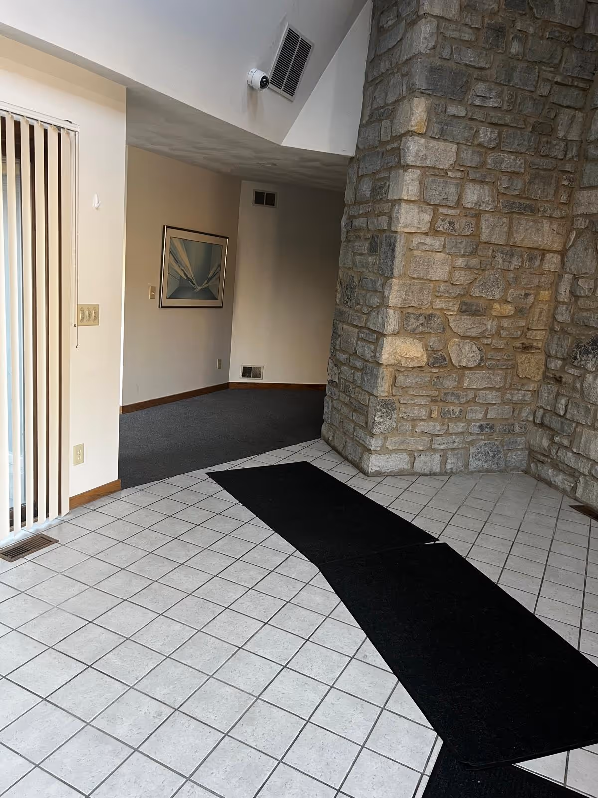 Interior lobby area with tiled floor, stone column, and sliding door entrance.