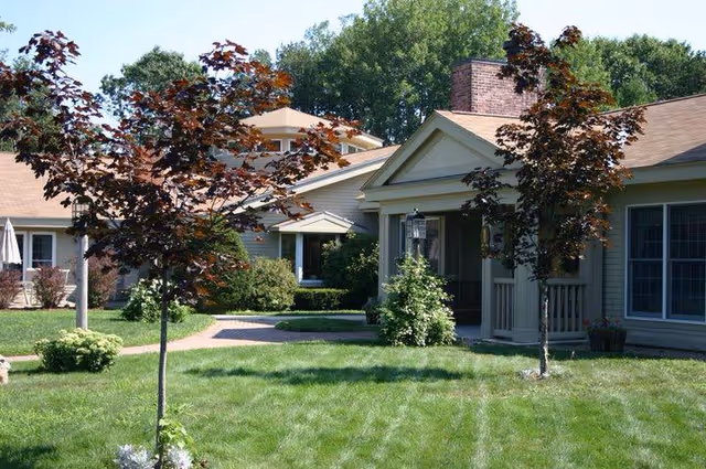 Senior living facility exterior with lawn, trees, and walkways in front of buildings