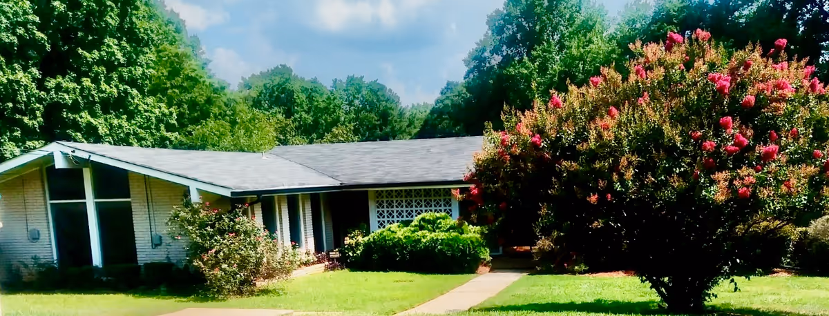 A single-story senior living facility with a manicured lawn, shrubs, and a flowering tree in front.
