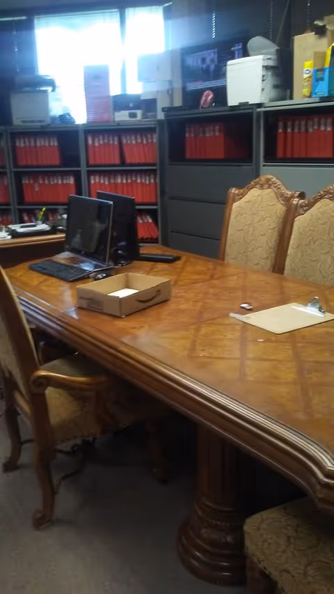 A wooden conference table with chairs, computers, and red filing cabinets in an office.