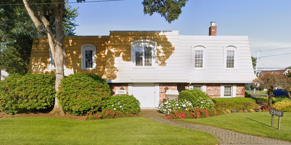 Sunlit front of a two-story senior living facility with manicured shrubs.