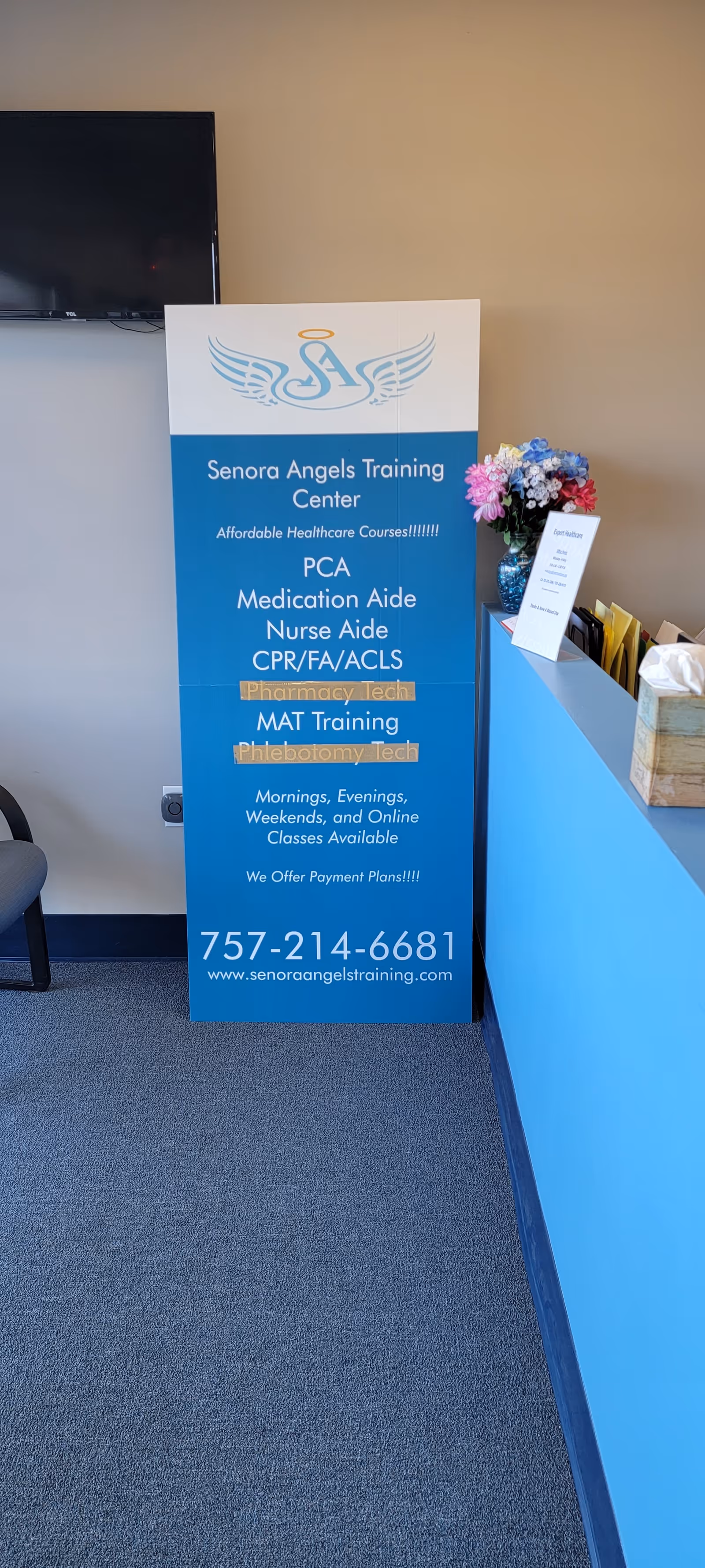 Tall blue training banner advertising healthcare courses beside a reception desk in a facility lobby.
