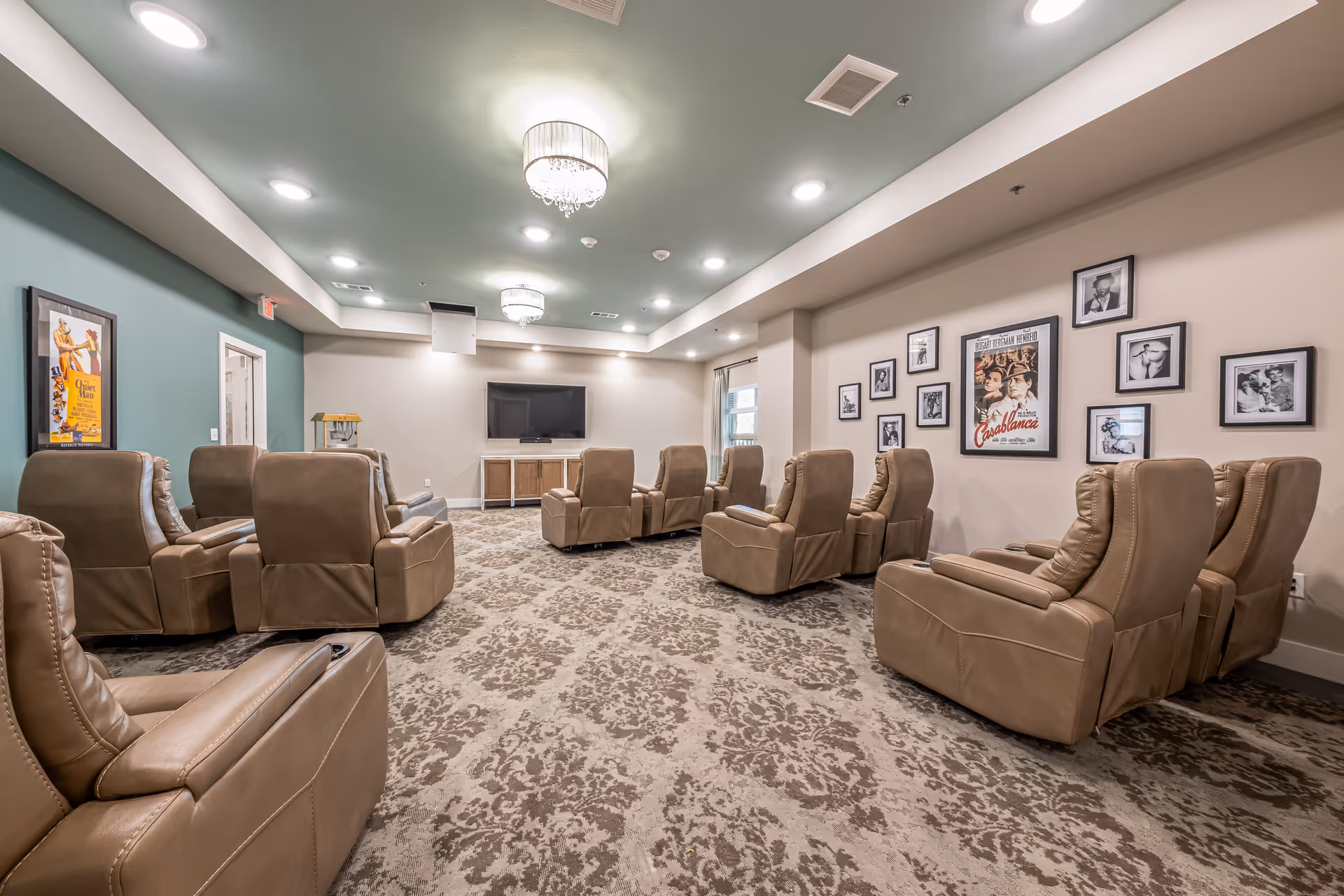 A spacious senior living lounge with beige recliners, carpet, wall art, and a TV.