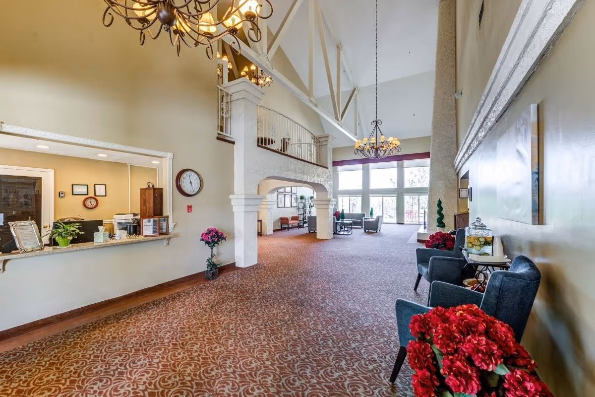 Spacious senior living facility lobby with chandeliers, reception desk, columns, and seating.