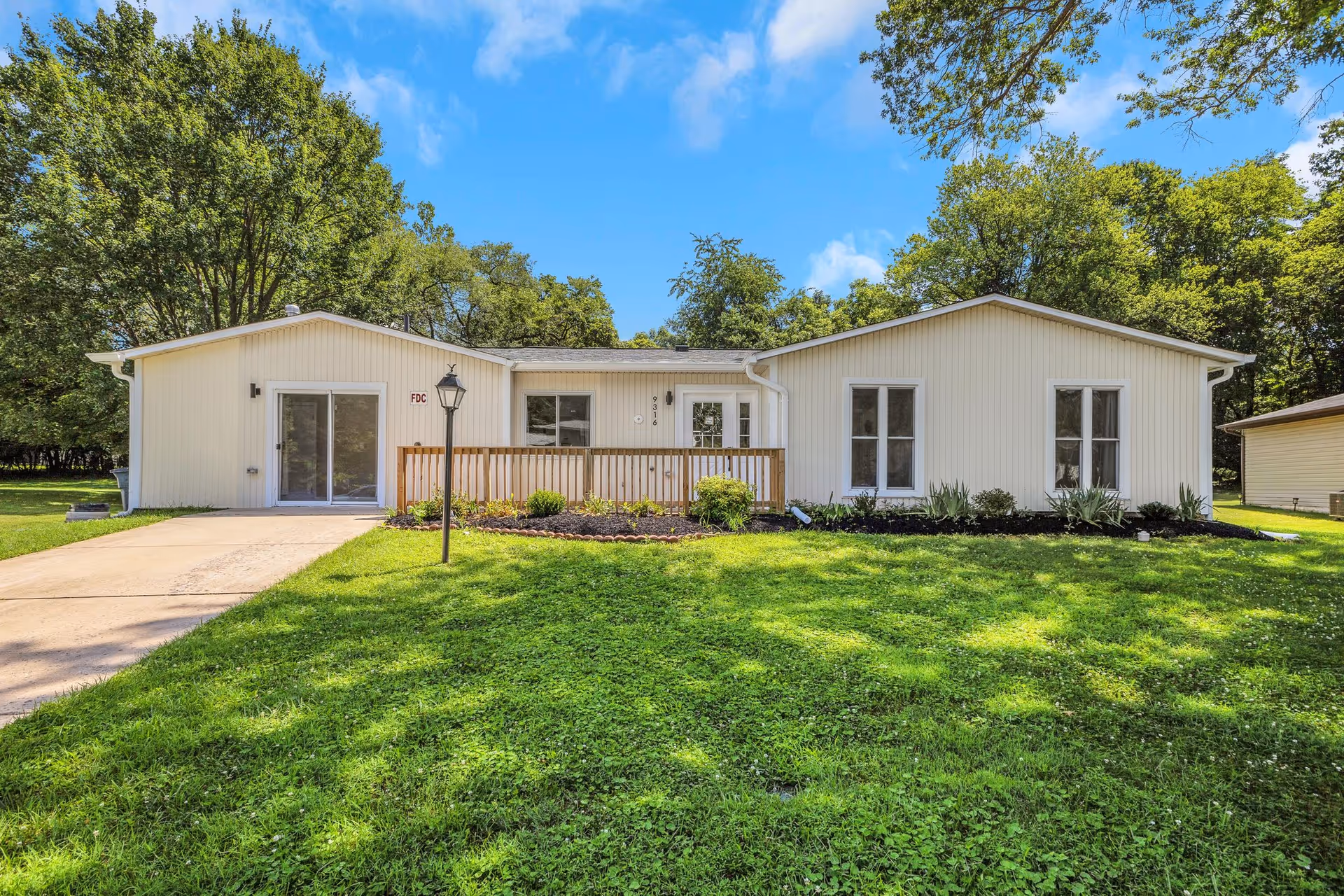 Single-story white care home exterior with a small front porch, green lawn, and blue sky.