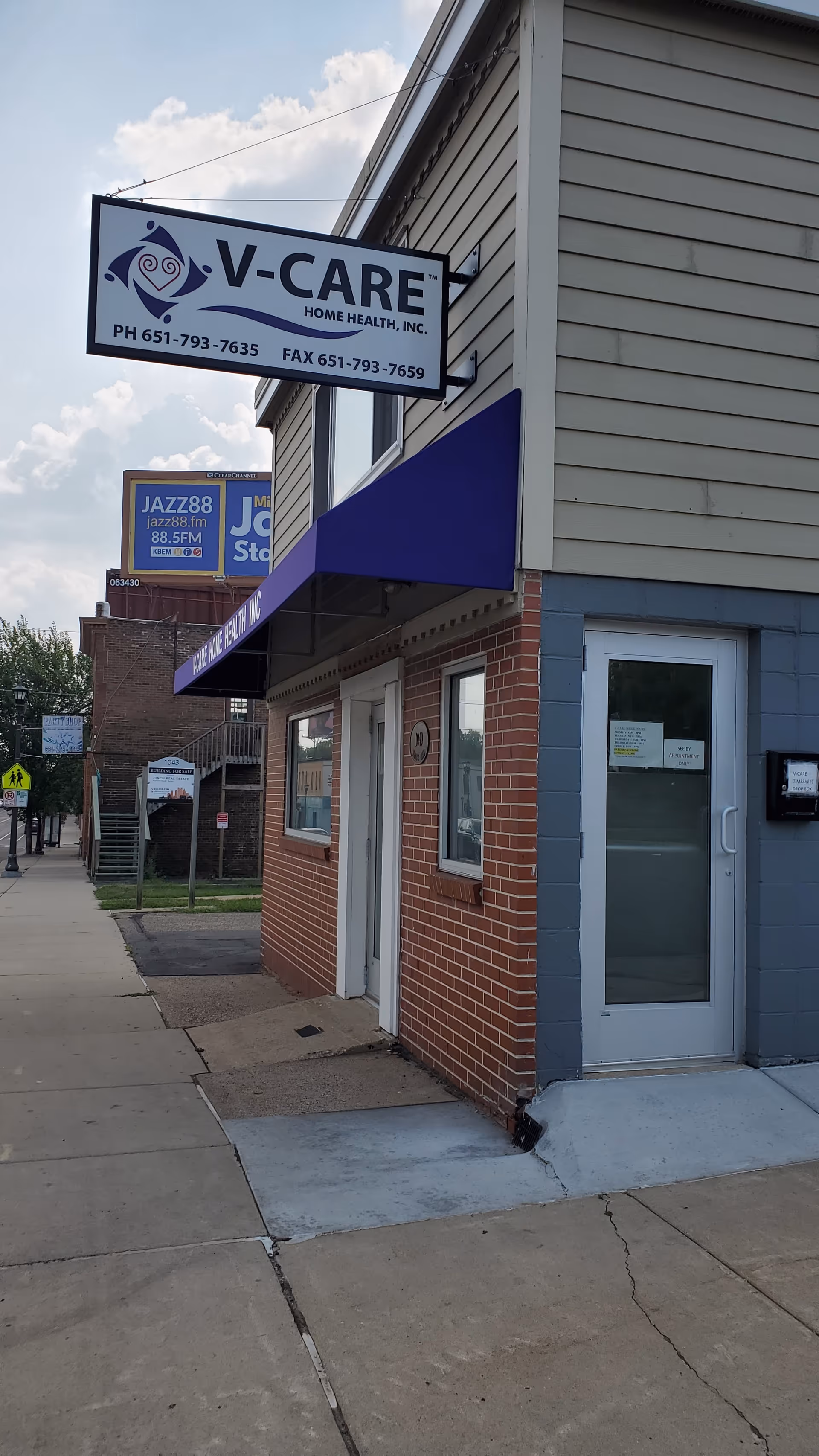 Exterior view of a brick building with a V-Care Home Health sign and storefront.